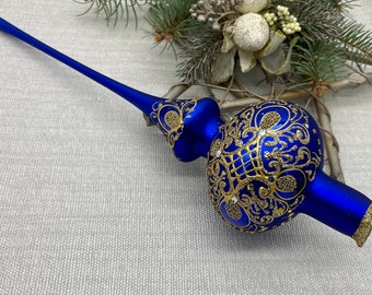 Könnte beinhalten: Ein königsblauer Weihnachtsbaumaufsatz mit goldenen Filigranarbeiten und funkelnden Akzenten. Der Glasschmuck hat einen länglichen Stiel und einen bauchigen Körper, ideal für festliche Dekorationen. Die goldenen Details verleihen Eleganz.