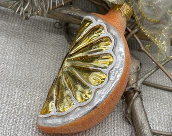 May include: Orange slice Christmas ornament with gold interior and silver trim. The ornament has a textured, glittery orange exterior and a gold-colored interior. The ornament is designed to look like a slice of citrus fruit.