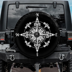 May include: Black Jeep with a spare tire cover featuring a white compass design with the letters N, S, E, and W.
