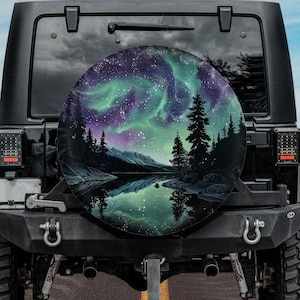 May include: A black Jeep with a spare tire cover featuring a colorful aurora borealis scene with a lake reflection. The scene includes trees and mountains.