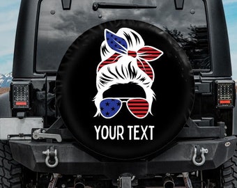 May include: A black spare tyre cover featuring a white silhouette of a woman wearing red, white and blue sunglasses and a headband. The text "YOUR TEXT" is printed below the image.