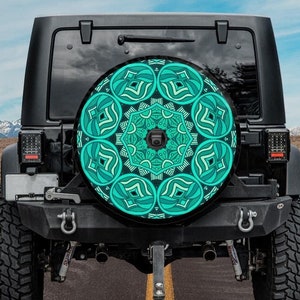 May include: A black Jeep with a teal and white mandala spare tire cover. The Jeep is parked on a paved road with yellow lines.