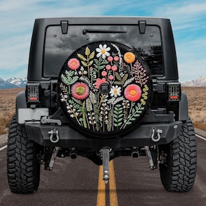 May include: Black Jeep with a spare tyre cover featuring an embroidered floral design in shades of pink, white, and green.