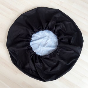 May include: A black drawstring bag with a white and blue patterned lining. The bag is gathered at the top and has a drawstring closure.