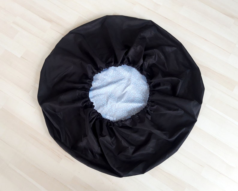 May include: A black, circular cover with a gathered edge, revealing a light blue interior patterned with small white dots. The cover is made of a smooth, possibly water-resistant material.
