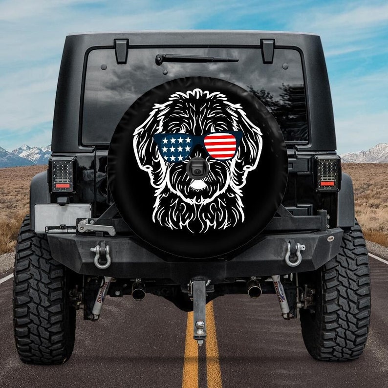 May include: A black Jeep with a spare tire cover featuring a white silhouette of a dog wearing sunglasses with an American flag design.