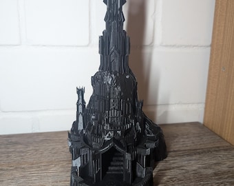May include: A black 3D printed model of the Dark Tower from the Lord of the Rings. The tower is tall and slender with a pointed top and a single eye on the top. The tower is surrounded by a base with a small entrance.