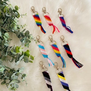 Peut inclure: Huit porte-clés en forme de bracelet d'amitié colorés avec des anneaux de clés argentés. Les bracelets sont faits de fils de différentes couleurs et présentent une variété de motifs.