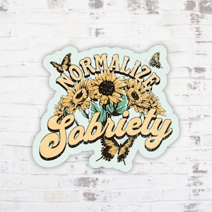 May include: A sticker with a light blue border featuring a bouquet of sunflowers and butterflies. The words "Normalize Sobriety" are written in a vintage-style font, with a distressed effect. The sunflowers are yellow and the butterflies are brown.