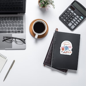 Puede incluir: Vista a&eacute;rea de un espacio de trabajo con un port&aacute;til, gafas, una taza de caf&eacute; sobre un posavasos de madera, una calculadora, un bol&iacute;grafo y un cuaderno con una pegatina "Extravagant Promises".