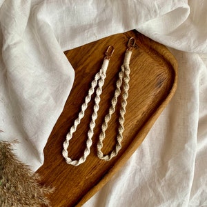 May include: Two white and brown macrame keychains with gold clasps on a wooden tray.