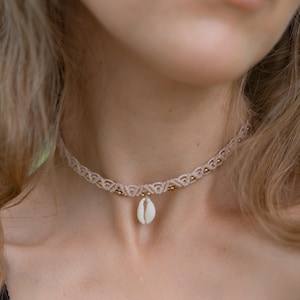 May include: A delicate beige macrame choker necklace with a small white seashell pendant.