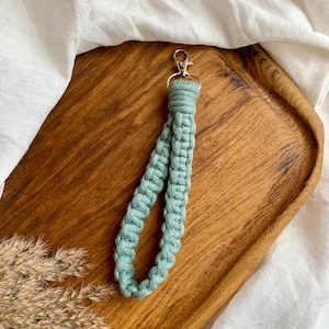 May include: A light green braided key chain with a silver metal clasp. The keychain is on a wooden surface.