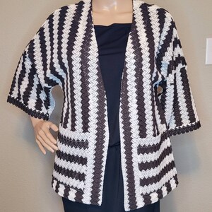 May include: A white and brown striped cardigan with a loose fit and long sleeves. The cardigan has a V-neck and two pockets.
