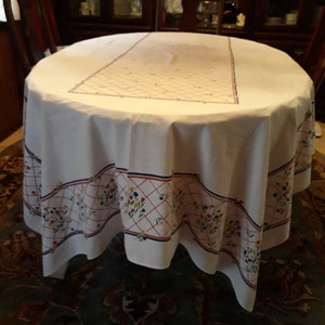 May include: White tablecloth with a red, blue, and yellow floral pattern around the border. The tablecloth has a white center with a subtle pattern.