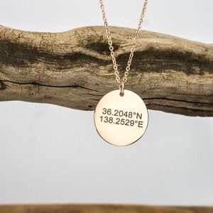 Puede incluir: Un collar de oro con un colgante redondo grabado con las coordenadas 36.2048° N 138.2529° E.