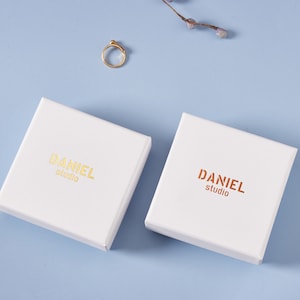 May include: Two white square boxes with the text "DANIEL studio" printed in gold and copper on the top of each box.