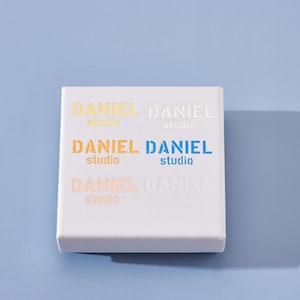May include: White box with the text "DANIEL studio" repeated four times in different colors, including orange, yellow, blue, and white.