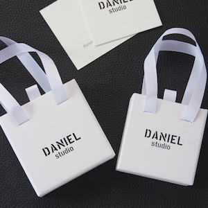 May include: Two white gift boxes with black handles and the text "DANIEL studio" printed on the front.
