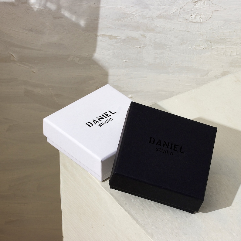 May include: Two square boxes, one white and one black, both with the text "DANIEL studio" printed on them.