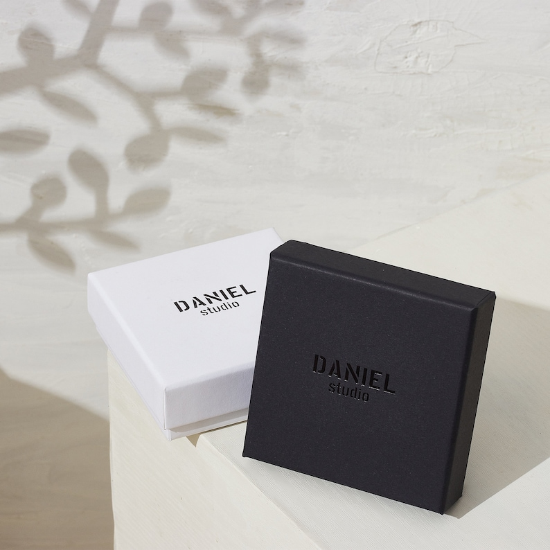 May include: Two square boxes, one white and one black, both with the text "DANIEL studio" printed on them.