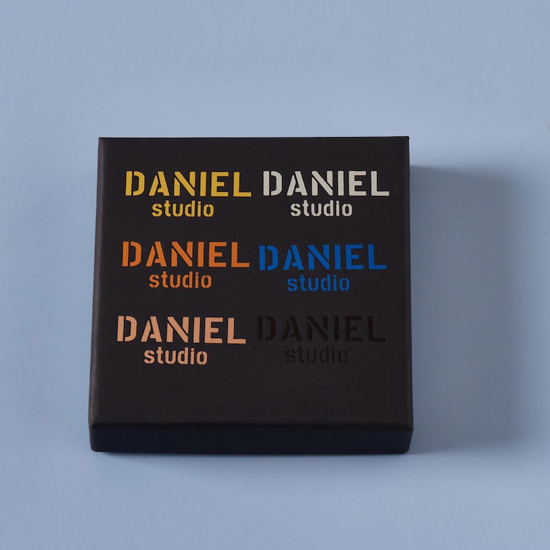 May include: Black box with the text "DANIEL studio" repeated six times in different colors: yellow, white, orange, blue, peach, and black.