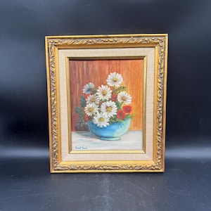 Naturaleza muerta floral vintage: margaritas en jarrón azul con marco dorado ornamentado.