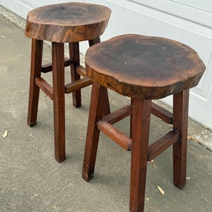 May include: Two wooden stools with round, natural wood tops and simple, sturdy legs. The stools are made from dark brown wood and have a rustic, farmhouse style.