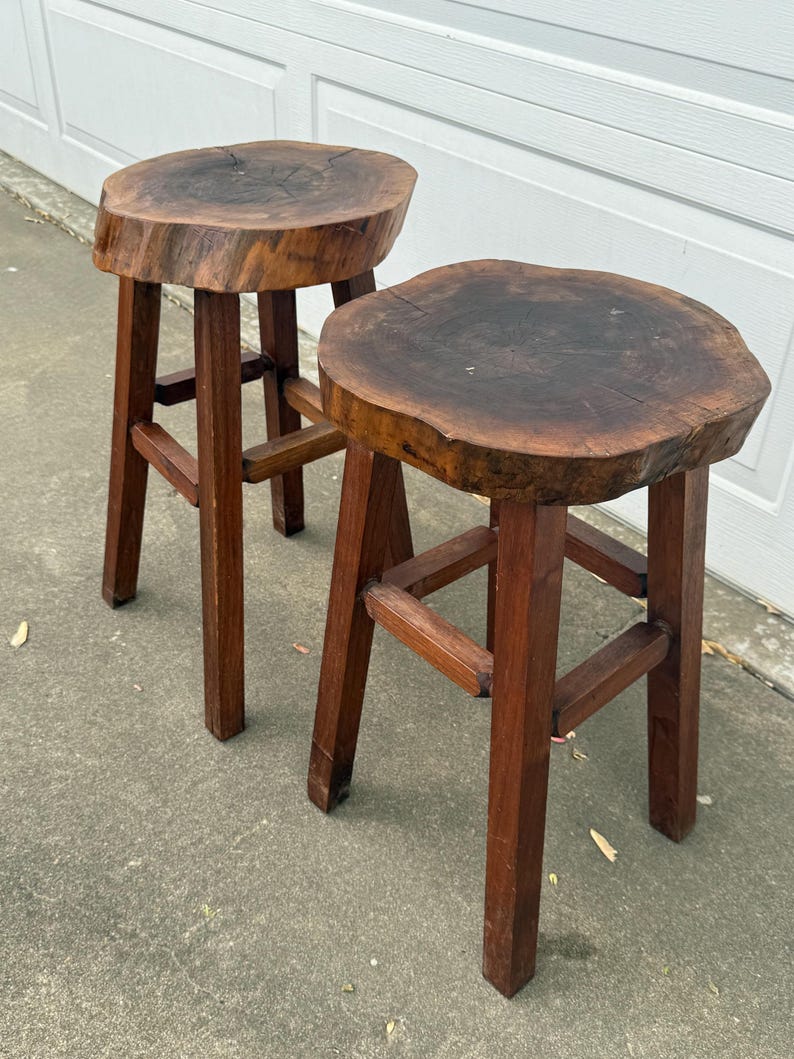 May include: Two wooden stools with round, natural wood tops and simple, sturdy legs. The stools are made from dark brown wood and have a rustic, farmhouse style.