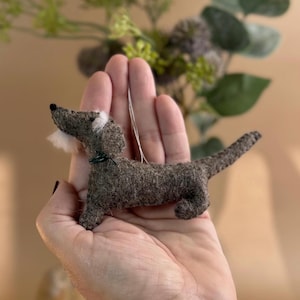 May include: A brown felt dachshund ornament with white fur on its face and a green ribbon around its neck.