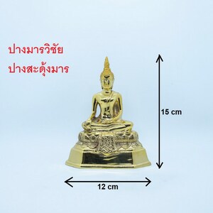 Puede incluir: Una estatua de Buda de color dorado sentada en una postura meditativa sobre una base de loto. La estatua mide 15 cm de alto y 12 cm de ancho.
