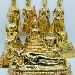 Puede incluir: Una colecci&oacute;n de nueve estatuas doradas de Buda en varias poses, incluyendo sentado, de pie y reclinado. Las estatuas est&aacute;n dispuestas en una plataforma escalonada con detalles intrincados.
