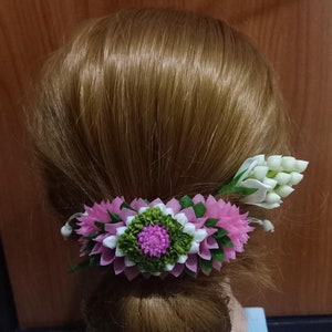 May include: A pink and white flower hair clip with green leaves. The clip is made of fabric and is designed to look like a real flower.