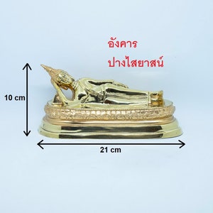 Puede incluir: Una estatua de Buda reclinado de color dorado sobre una base decorativa. La estatua mide 10 cm de alto y 21 cm de ancho. La base tiene detalles intrincados.