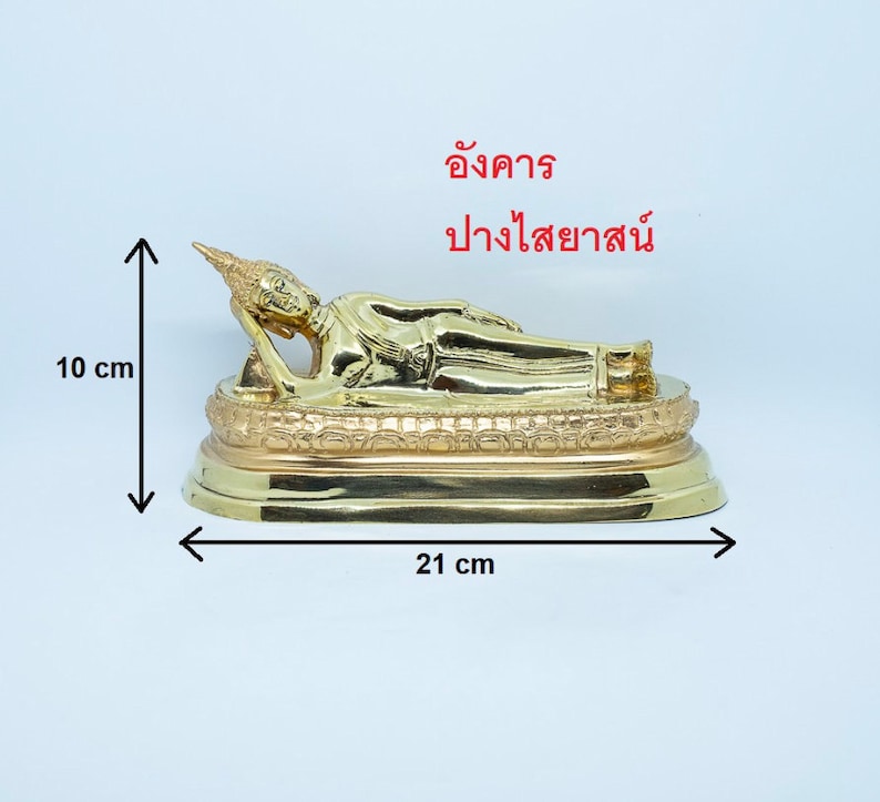 Puede incluir: Una estatua de Buda reclinado de color dorado sobre una base decorativa. La estatua mide 10 cm de alto y 21 cm de ancho. La base tiene detalles intrincados.