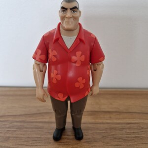 May include: A plastic action figure of a man wearing a red short-sleeved shirt with orange floral print and brown trousers. The figure has a short, grey, spiky hairstyle and a serious expression.