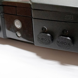 May include: A black Xbox console with the Microsoft logo and the word "Xbox" printed on the front. The console has a series of vents on the right side.