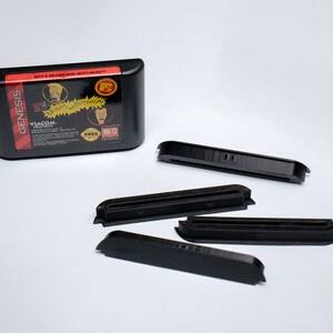 May include: A black Sega Genesis game cartridge for the game "Beavis and Butt-Head" with the text "It's Beavis and Butt-Head" and "VIACOM" printed on the label. Four black plastic cartridge holders are also shown.