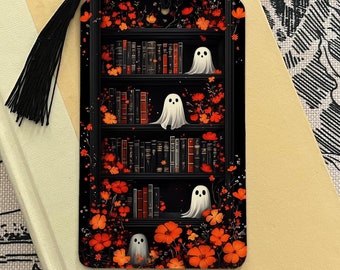May include: A black and white bookmark with a bookshelf filled with books and four white ghosts. The bookshelf is surrounded by orange flowers. The bookmark has a black tassel.