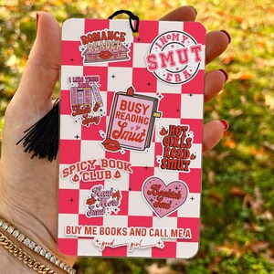 May include: Pink and white chequered bookmark with various stickers featuring the text "Romance Reader", "I Like Thick & Spicy", "Busy Reading Smut", "Hot Girls Read Smut", "Spicy Book Club", "Read More Smut", "Bookish Soul", "In My Smut Era", and "Buy Me Books and Call Me A Good Girl".