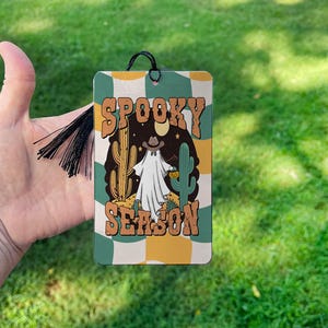 May include: A green, yellow, and white bookmark with a ghost wearing a cowboy hat and the text "Spooky Season".