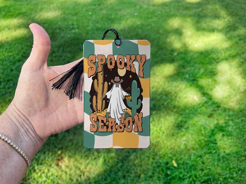 May include: A green, yellow, and white bookmark with a ghost wearing a cowboy hat and the text "Spooky Season".