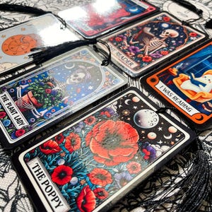 May include: A set of ten tarot cards with black tassels. The cards feature colorful illustrations with titles such as "The Plant Lady", "The Poppy", "I Was Reading", "Wheel of Fortune", and "Sorry I Ghosted".