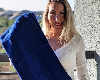 May include: A woman holds a large, dark blue towel in front of her. The towel is folded in half and is draped over her shoulder.