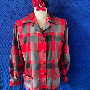 May include: A vintage red, black, and grey plaid jacket with a collared neckline, three buttons, and two front pockets. The jacket is displayed on a mannequin with a red flower and black accessory.