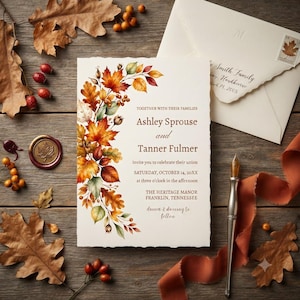 May include: A wedding invitation card with deckled edges featuring a watercolour illustration of autumn leaves and berries on the left side. The text reads: Together with their families, Ashley Sprouse and Tanner Fulmer invite you to celebrate their union.