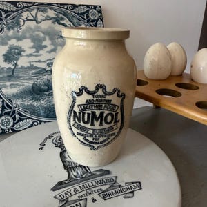 May include: A cream-coloured ceramic jar with a dark blue printed label that reads TONIC AND NERVINE LECITHIN FOOD NUMOL BODY BUILDER DIGESTIVE & APPETISER FOR CHILDREN & ADULTS. The jar has a wide mouth and a smooth, cylindrical body shape.