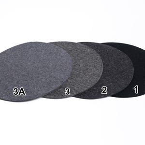 Puede incluir: Cuatro posavasos circulares de fieltro dispuestos en fila, mostrando un degradado de tonos grises de claro a oscuro. Cada posavasos est&aacute; etiquetado con texto blanco: 3A para el gris claro, 3 para el gris medio, 2 para el gris oscuro y 1 para el negro.