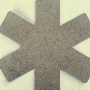 Può includere: Un sottopentola in feltro grigio a forma di stella a sei punte. Il sottopentola è progettato per proteggere le superfici dal calore.