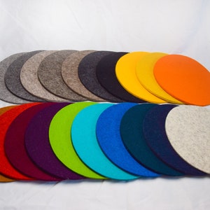 May include: A set of 15 round felt coasters in various colours, including brown, red, purple, green, blue, grey, yellow, and orange. The coasters are arranged in a semi-circle.